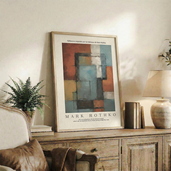 May include: Abstract geometric poster with orange, blue, and gray rectangular blocks in wooden frame, displayed on rustic wooden sideboard alongside potted fern, ceramic vase, stacked books, and beige armchair in warm neutral living room setting