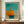 May include: Framed abstract art print in warm orange, turquoise blue, and cream tones displayed on wooden credenza beside white ceramic vase and stacked books. The artwork features geometric color blocks with soft, blended edges in Rothko's signature style. Modern interior setting with white paneled walls and natural lighting.