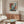a modern living room with a large abstract painting hanging on the wall above a wooden cabinet. The room has a white sofa, a glass coffee table, and a lamp on a side table.