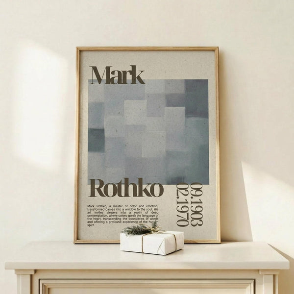 May include: Framed art print featuring Mark Rothko's name and exhibition details in serif typography, with abstract geometric shapes in muted gray and blue tones. Natural wood frame displays on light wooden surface alongside small white wrapped gift with evergreen sprig. Minimalist gallery wall styling against cream background with soft natural lighting.