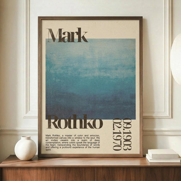 May include: Framed poster with blue gradient watercolor artwork and "Mark Rothko" typography, displayed on wooden credenza next to white ceramic vase and stacked books against cream paneled wall. The print features soft blue tones transitioning from light to deep blue with descriptive text below in brown wooden frame.