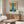 May include: Abstract art poster with blue vertical stripe down center and orange-yellow sections on sides, displayed above wooden sideboard in modern living room. White sculptural chair and glass coffee table in foreground. Poster shows French text and Mark Rothko attribution at bottom with thin wooden frame.