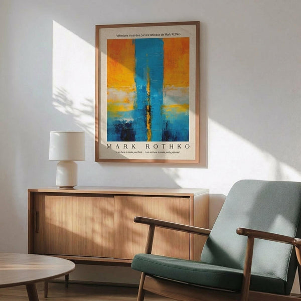 May include: Abstract art poster with vertical blue stripe through orange and yellow color fields, displayed in wooden frame above mid-century modern credenza. Room features mint green upholstered chair with wooden arms, white ceramic table lamp, and warm sunlight casting shadows on white wall.