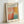 May include: Framed exhibition poster featuring abstract colorful artwork with soft brushstrokes in coral pink, orange, yellow, and turquoise blue. Text reads "MARK ROTHKO" at top with "Rothko Art Gallery, New York City" and exhibition details below. Shows April 15 - July 30, 2023 dates and 6:00 PM time. Light wooden frame sits against white wall casting gentle shadow.