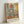 Framed abstract art print featuring geometric shapes in muted tones of blue, orange, yellow, and beige with soft brushwork and layered rectangular forms. The artwork is displayed in a light wooden frame with "MARK ROTHKO" and French text at the bottom, leaning against a white wall on a light surface.