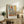May include: Framed abstract art print in warm earth tones featuring geometric shapes in orange, blue, and beige, displayed on rustic wooden sideboard alongside fern plant, ceramic vase, and leather armchair in neutral-toned living room setting.