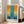 May include: Framed abstract art poster leaning against white wall next to beige sofa in bright living room. Artwork features vertical blue brushstrokes over orange and yellow background with darker blue sections at bottom. French text at top, artist name and quote at bottom. Natural wood frame, hardwood floors visible.
