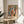 May include: Framed abstract art print in wooden frame displaying colorful organic shapes in blues, oranges, greens, and yellows with black dots and flowing forms, titled "MATISSE" at bottom. Print sits on round wooden side table next to beige upholstered chair with plant leaves visible in soft natural lighting.
