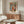 May include: Colorful abstract art print with organic shapes, wavy lines, and polka dots in blues, oranges, greens, and yellows, displayed in thin wooden frame above mid-century walnut credenza. Modern living room setting with white curved chair, glass oval coffee table, and minimalist white table lamp.