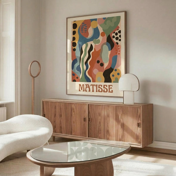 May include: Colorful abstract art print with organic shapes, wavy lines, and polka dots in blues, oranges, greens, and yellows, displayed in thin wooden frame above mid-century walnut credenza. Modern living room setting with white curved chair, glass oval coffee table, and minimalist white table lamp.