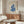 May include: Framed Matisse-inspired poster with blue coral-like cutout shapes on cream background, displayed above walnut credenza in modern living room with white sculptural chair, glass coffee table, and warm natural lighting