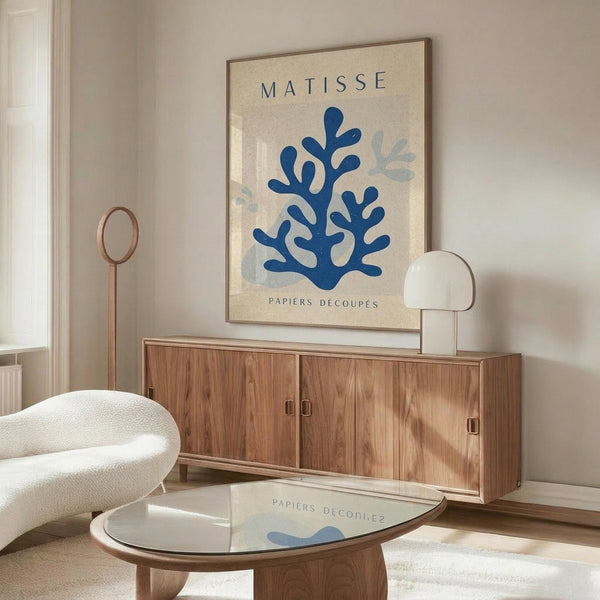 May include: Framed Matisse-inspired poster with blue coral-like cutout shapes on cream background, displayed above walnut credenza in modern living room with white sculptural chair, glass coffee table, and warm natural lighting