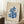 May include: Framed poster with cream background featuring blue coral-like cut-out shapes in Matisse style, displaying "MATISSE" and "PAPIERS DÉCOUPÉS" text. Light wood frame leaning against white wall corner near wooden side table with white coffee cup and beige throw blanket on textured rug.