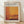 May include: Framed exhibition poster featuring Mark Rothko artwork with warm orange, yellow, and brown geometric color blocks. Light wood frame displays gallery information and exhibition dates. Poster leans against white wall on light wooden floor with soft natural lighting and fabric shadows.