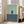 May include: Framed abstract art print with sage green upper section, darker teal lower section, yellow side panels, and suspended dark blue rectangle. Light wood frame leaning against white wall beside beige upholstered sofa in bright, windowed living room with hardwood floors.