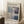 May include: Framed exhibition poster featuring Mark Rothko's abstract color field painting with blue, purple, cream and white rectangular blocks. Light wood frame leaning against white wall corner on textured cream rug, beside wooden side table with white coffee cup and saucer, cozy beige throw blanket visible at edge.