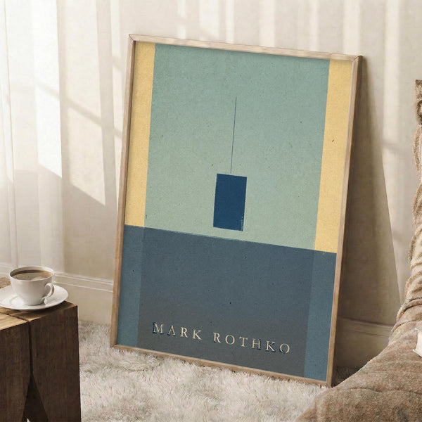 May include: Framed abstract art print leaning against white wall in cozy living room setting. Artwork features geometric composition with pale green background, dark blue rectangle, and yellow border accents. Natural wood frame complements minimalist decor with coffee cup on wooden side table and textured cream rug below.