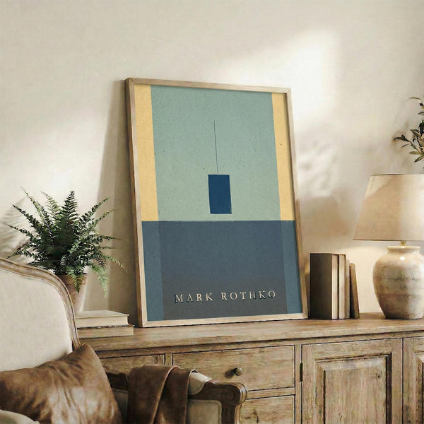 May include: Framed abstract art print with geometric color blocks in sage green, navy blue, and cream tones displayed on rustic wooden sideboard. Room setting shows leather armchair, potted fern, ceramic vases, and stacked books creating cozy living space with neutral walls and warm lighting.