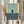 May include: Hands holding framed abstract art print with geometric color blocks in sage green, navy blue, and cream yellow tones, displayed next to dried pampas grass against soft neutral curtained background in natural lighting