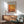 a living room with a wooden cabinet, a green armchair, and a wooden coffee table. Above the cabinet, there is a framed poster of Mark Rothko's artwork displayed on the wall.