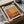 a framed poster or artwork displayed in a cardboard box, with a clear plastic sleeve on top.