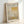 May include: Framed exhibition poster featuring Mark Rothko's abstract artwork in warm yellow, orange, and neutral tones with geometric color blocks. The poster displays gallery information and exhibition dates April 15 - July 30, 2023. Light wood frame against white wall with soft natural lighting creating gentle shadows.