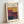 May include: Framed exhibition poster featuring Mark Rothko's abstract color field artwork with geometric blocks in warm yellows, deep reds, purples, and dark blues. Light wooden frame displayed against white wall, showing gallery text and exhibition dates April 15 - July 30, 2023 at 6:00 PM. Minimalist museum-style design with cream background highlighting the rich, layered paint textures of the featured artwork.
