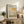 May include: Framed art poster featuring abstract color blocks in warm yellows, oranges, and neutral tones displayed on rustic wooden sideboard. Scene includes leather armchair, potted fern, ceramic vases, and stacked books in cozy living room with white walls and natural lighting.