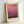 May include: Framed art print featuring abstract gradient from coral pink at top transitioning through magenta to deep burgundy at bottom, displayed in light wooden frame with white matting against white wall, leaning on surface with soft natural lighting creating subtle shadows