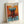 May include: Framed abstract art print in light wood frame leaning against white wall. The artwork features bold brushstrokes in vibrant orange, turquoise blue, and deep red colors with painterly texture. The composition shows horizontal bands of color with expressive, loose brushwork typical of abstract expressionist style.