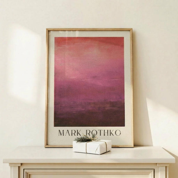 May include: Abstract gradient artwork in warm wood frame leaning against cream wall on light wooden surface. Image shows coral pink at top transitioning through magenta to deep burgundy and brown at bottom with horizontal brushstroke texture. Small white wrapped gift with green sprig sits beside frame. Soft natural lighting creates gentle shadows.