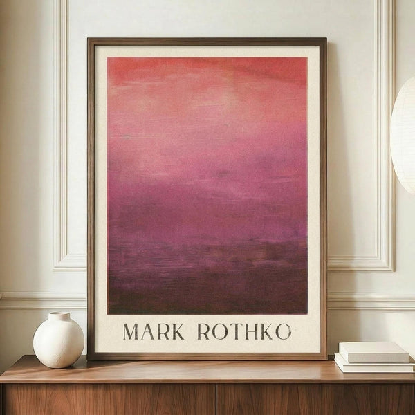 May include: Framed abstract art print displayed on wooden sideboard featuring gradient wash from coral pink at top transitioning to deep burgundy and dark brown at bottom. Minimalist poster with artist name in serif font below artwork. Styled with white ceramic vase and stacked books against cream paneled wall.