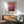 May include: Framed Mark Rothko poster with pink and burgundy abstract color fields hanging above modern wooden credenza. Mid-century sage green upholstered armchair with wooden frame sits nearby. White ceramic table lamp and round coffee table visible. Warm natural lighting creates geometric shadows on white wall.