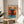 May include: Framed abstract art poster featuring vibrant orange and turquoise blue brushstrokes in Rothko's signature color field style, displayed on a round wooden side table next to a cream upholstered chair. Soft natural lighting creates shadows across the minimalist white-walled room setting with a plant visible in the corner.