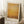 May include: Framed abstract art print in warm golden and amber tones with soft, blended brushwork effects, displayed leaning against white wall corner on textured cream rug. Natural wood frame surrounds the atmospheric artwork. Small wooden side table with white coffee cup visible in scene.