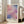 May include: Abstract watercolor art print in light wood frame leaning against white wall next to beige sofa. Artwork features soft brushstrokes in pink, purple, and blue tones with "MARK ROTHKO" text below. Bright room setting with large windows, hardwood floors, and natural lighting creating gentle shadows on the wall.