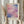 May include: Person holding framed abstract art print with soft gradient colors blending from coral pink to deep blue and purple in pixelated blocks. Light wood frame with cream matting displays artist name below artwork. Dried pampas grass stems held in other hand against neutral beige curtained background.