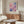 May include: Abstract watercolor artwork with soft pink, purple, and blue rectangular color blocks in thin wooden frame, displayed above mid-century modern walnut credenza in minimalist living room with cream walls, white sculptural chair, glass coffee table, and modern table lamp