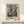 May include: Framed abstract art print featuring geometric kitchen vessels in muted teal, coral, and beige tones, displayed on light wood console table beside small white wrapped gift with twine and greenery sprig against cream wall