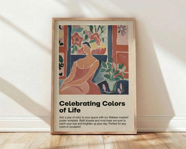May include: Framed art print leaning against white wall on light wood floor. The poster features a Matisse-inspired illustration of a woman in coral dress sitting among potted plants and flowers in bold, flat colors including coral, navy, green, and cream. Below the artwork is black text reading "Celebrating Colors of Life" with descriptive paragraph. Natural wood frame with beige matting. Soft window light creates diagonal shadows across the white textured wall.
