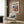 May include: Cream armchair with geometric patterned pillow positioned next to wood paneled wall. Framed colorful abstract art poster featuring flowing organic shapes in blues, oranges, and reds with "matisse modernist" text. Brass floor lamp and dark side table with open book complete the modern living room setting with natural lighting.