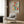 May include: Colorful Matisse-inspired floral poster with abstract flowers in red, orange, teal, yellow and pink tones, displayed in light wood frame on wood panel wall above beige upholstered armchair with geometric patterned pillow, brass floor lamp and dark round side table with open book visible in modern neutral living room setting