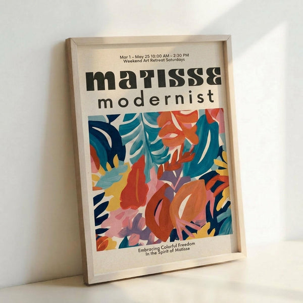 May include: Framed poster with "Matisse modernist" text and vibrant abstract botanical artwork featuring flowing leaves and organic shapes in teal, coral, orange, pink, and yellow colors. Light wood frame leans against white wall, showing colorful cut-out style design reminiscent of Matisse's paper collages. Bottom text reads "Embracing Colorful Freedom In the Spirit of Matisse" with exhibition dates at top.