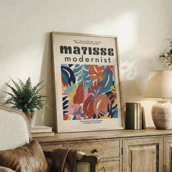 May include: Framed modernist art poster with abstract colorful shapes in blues, reds, oranges and yellows, displayed on rustic wooden sideboard alongside fern plant, ceramic vases, and books in cozy living room with cream armchair and neutral walls