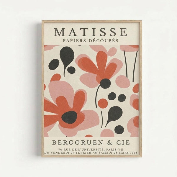 A framed vintage exhibition poster featuring Matisse's cut-out paper artwork in coral, pink, and black organic shapes resembling flowers and leaves against a cream background. The poster shows gallery information for Berggruen & Cie in Paris, dated 1958. The artwork is displayed in a thin natural wood frame against a white wall.