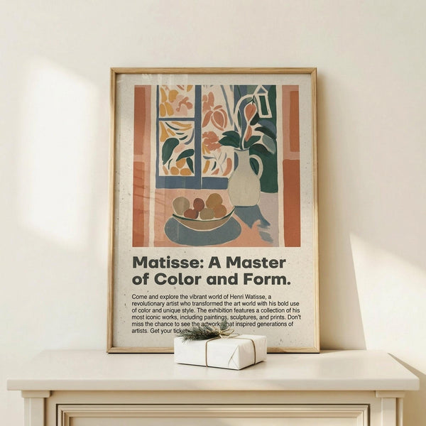 May include: Framed exhibition poster featuring Matisse-style still life with window, vase of flowers, and fruit bowl in warm earth tones and blues. Displayed on light wood surface alongside small wrapped gift with twine and greenery sprig against cream wall. Natural lighting creates soft shadows on the minimal modern interior setting.