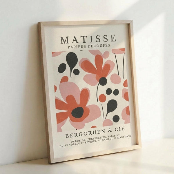 May include: Framed art print featuring Matisse-style abstract floral design in coral pink, salmon, and black organic shapes on cream background, displayed in light wood frame leaning against white wall with soft natural lighting and shadow