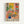 Colorful art print in light wood frame featuring an interior scene with tropical plants in decorative vases, a patterned armchair, and geometric wall art tiles. The illustration uses vibrant yellows, pinks, blues and greens in a flat, modern style reminiscent of mid-century design. Bold black text reading "MATISSE" appears at the bottom of the composition.
