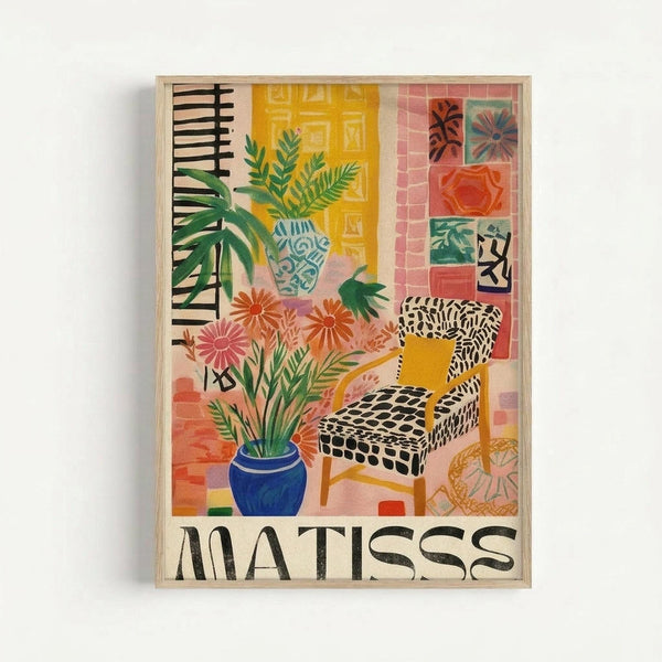 Colorful art print in light wood frame featuring an interior scene with tropical plants in decorative vases, a patterned armchair, and geometric wall art tiles. The illustration uses vibrant yellows, pinks, blues and greens in a flat, modern style reminiscent of mid-century design. Bold black text reading "MATISSE" appears at the bottom of the composition.