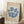May include: Framed art print leaning against white wall corner on textured white rug. Poster features blue coral-like branching design on cream background with "MATISSE" text at top and gallery information below. Light wood frame, displayed next to wooden side table with white coffee cup and saucer. Soft natural lighting creates gentle shadows.